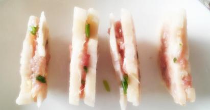 把准备好的肉馅用拇指捏进藕片里面，放入盘中。