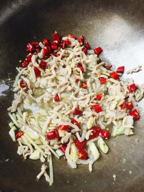 肉丝泛白之后，放入姜丝、大蒜、干辣椒翻炒均匀，倒入适量的料酒