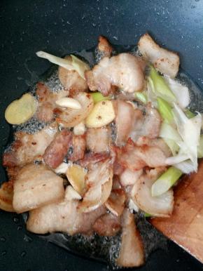 放入葱姜蒜继续煸炒，待肉微卷，油脂大部分被煸出后，倒入生抽老抽翻炒均匀