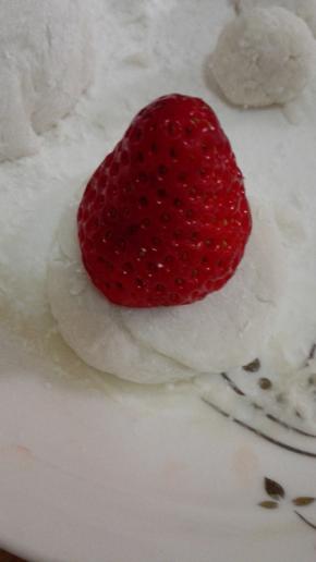 等糯米皮晾凉不烫手之后取出一小块，压成圆形，将草莓放在糯米皮上，手沾一些糯米粉，将糯米皮包裹上草莓