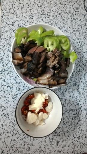 腊肉过水煮熟切片，青椒、小米辣切圈、大蒜切片备用