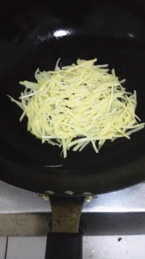 锅内放入少量的油，油热放入土豆丝，用铲子压成饼的形状