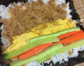 在米饭上依次摆放黄瓜条，胡萝卜条，蛋皮和肉松