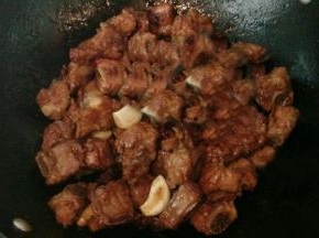 放入排骨，八角，蒜瓣和姜片，倒入生抽，炒至排骨均匀上色