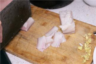 将五花肉煮至快好时（筷子可插入即可），将其取出放菜板上冷却，将肉切成薄片，姜、蒜切片，葱切成斜段。