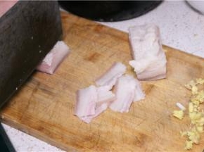 将五花肉煮至快好时（筷子可插入即可），将其取出放菜板上冷却，将肉切成薄片，姜、蒜切片，葱切成斜段。