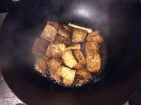 豆腐煎成外皮金黄，倒入蚝油、酱油和清水，放上1根葱，小火翻炒烧制