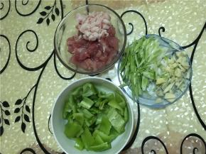 肉切薄片，用料酒、盐和生粉腌制15分钟, 蒜头拍碎，青椒切丁。
