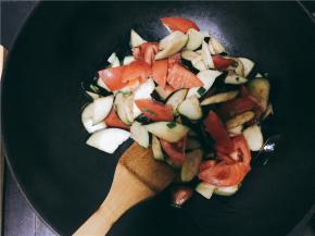 锅中到油，油热后将小葱葱白部分与蒜瓣倒入锅中炒香并迅速将茄子倒入锅中翻炒，茄子变色后倒入西红柿再次进行翻炒，此时可以加入调料继续翻炒。