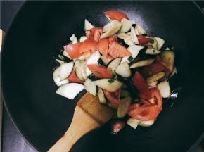 锅中到油，油热后将小葱葱白部分与蒜瓣倒入锅中炒香并迅速将茄子倒入锅中翻炒，茄子变色后倒入西红柿再次进行翻炒，此时可以加入调料继续翻炒。