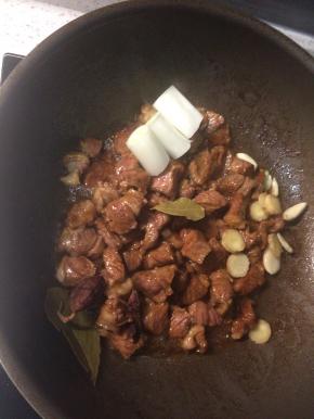 牛腩翻炒至所有肉块都裹上焦糖色并微微出油后，下入八角、葱段、姜片和蒜瓣，如有的话可以加一个草果和两片香叶，翻炒均匀。