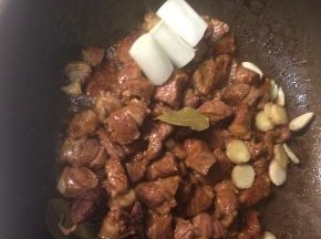 牛腩翻炒至所有肉块都裹上焦糖色并微微出油后，下入八角、葱段、姜片和蒜瓣，如有的话可以加一个草果和两片香叶，翻炒均匀。