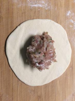 醒好的面撒上干面粉和成光滑的面团，再均匀地分成小剂子，小剂子擀成薄片后，放上之前拌好的肉馅。