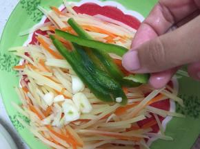 将胡萝卜土豆丝沥水装盘，大蒜碎和青椒丝置于土豆胡萝卜丝上
