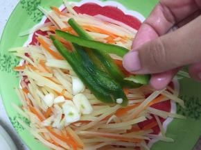 将胡萝卜土豆丝沥水装盘，大蒜碎和青椒丝置于土豆胡萝卜丝上
