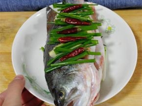 铺一层姜片葱段在盘底，鱼肚内塞入姜片，放入蒸锅内蒸5分钟，倒去汁液，淋上蒸鱼鼓油，将葱姜均匀铺满鱼，依照个人喜好加入干辣椒