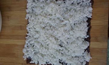 将紫菜铺在案板上，拌好的米饭铺在上面并压实