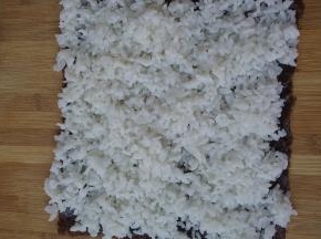将紫菜铺在案板上，拌好的米饭铺在上面并压实
