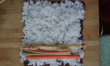 将黄瓜条、火腿条、胡萝卜条、蛋条放在压好的米饭上