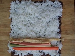 将黄瓜条、火腿条、胡萝卜条、蛋条放在压好的米饭上