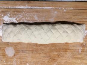 将糯米饭均匀地铺在面片中间，两头留一点边，四边刷一点清水将糯米饭包起来成长条形，包好后翻过来用刀在表面划上格子