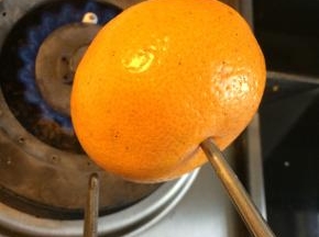 拿一个新鲜的桔子，取一根筷子从桔子中间的凹陷处插入，燃气灶开最小火，将桔子放在火上烤，不断旋转让桔子均匀受热。