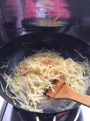 锅内放入适量油，放入葱花等调料，把土豆放入锅内翻炒。