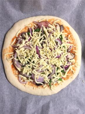 先撒上一层马苏里拉奶酪，再均匀地铺上火腿片，然后再放上香菇、青椒和洋葱