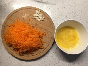 胡萝卜擦成细丝，蒜切蒜片，鸡蛋加少许盐打散备用