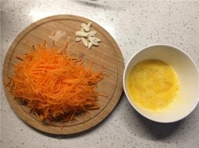 胡萝卜擦成细丝，蒜切蒜片，鸡蛋加少许盐打散备用