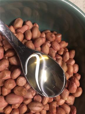 花生米放在大碗里，倒一勺食用油拌匀，使每颗花生米表面都裹上一层薄油