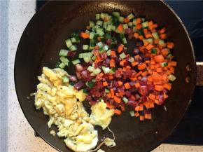 将炒好的鸡蛋拨到一边，下入腊肠黄瓜胡萝卜丁翻炒