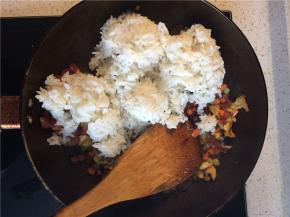 炒至腊肠透亮出油，下入冷米饭，用铲子压碎结块的米饭，使米饭粒粒分开