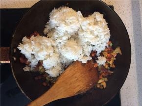 炒至腊肠透亮出油，下入冷米饭，用铲子压碎结块的米饭，使米饭粒粒分开