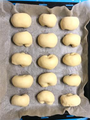 松弛好的小面团用擀面棍擀开后再卷起来，两头弯回来压在下面，放入铺油纸的烤盘