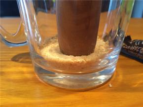 取一个透明的杯子，先放一层手指饼碎，用擀面杖一端轻轻压平