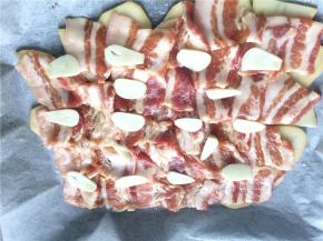 再平铺上一层腌好的五花肉片，均匀地撒上蒜片姜丝。