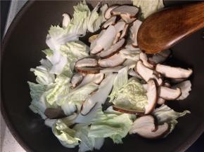 下入香菇和白菜翻炒一分钟后，加入食盐继续翻炒至蔬菜变软