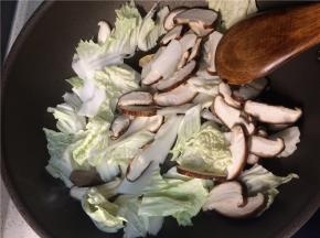 下入香菇和白菜翻炒一分钟后，加入食盐继续翻炒至蔬菜变软
