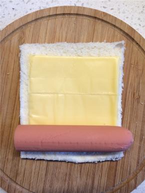 在吐司的中间放上一片芝士，火腿肠放在一端，从放火腿肠的一端卷起来