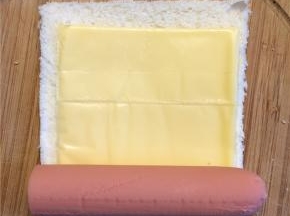 在吐司的中间放上一片芝士，火腿肠放在一端，从放火腿肠的一端卷起来