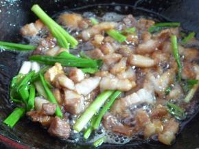 冰糖融化看不到颗粒时，将葱段、姜片放入，随后放入五花肉块翻炒几下给五花肉上色