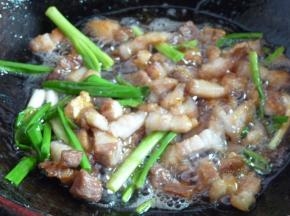 冰糖融化看不到颗粒时，将葱段、姜片放入，随后放入五花肉块翻炒几下给五花肉上色