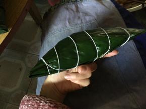 稍微将边缘散出的米拨回中心，将两边的叶子合上，随后用手指压出一端的边线，将一端叶子往下折，整理边线；换一端重复同样动作收折。最后用细毛线将粽子一圈圈缠好扎起。粽子就做好了！！！