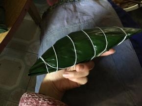 稍微将边缘散出的米拨回中心，将两边的叶子合上，随后用手指压出一端的边线，将一端叶子往下折，整理边线；换一端重复同样动作收折。最后用细毛线将粽子一圈圈缠好扎起。粽子就做好了！！！