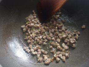 5、起锅热油爆香葱花，下入猪肉丁翻炒至变白。