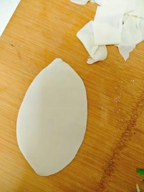 取一张饺子皮。用擀面杖擀薄后，用手从中间将面皮撕开，变成扯面