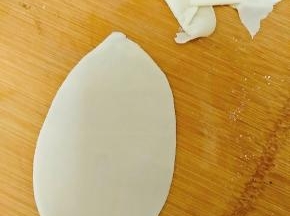 取一张饺子皮。用擀面杖擀薄后，用手从中间将面皮撕开，变成扯面