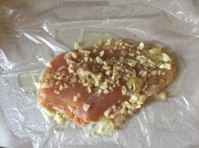 在保鲜膜上放上鸡胸肉，将拌好的料汁倒上，加入盐、糖、胡椒粉抹匀。