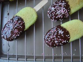 把脱模后的蛋糕冰棒沾上融化的巧克力放在烤网上，下面放上烤盘。余下少量的巧克力可装入裱花袋里，剪一点小口在冰棒上画Z字，撒上彩色糖珠晾凉即可。烤盘里的巧克力也不要浪费掉，待晾凉后收集起来可重复使用哦。